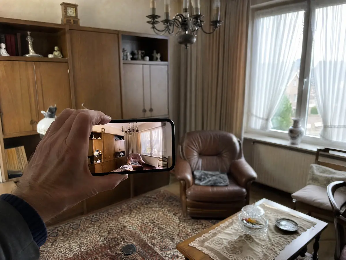 Iemand fotografeert met een gsm de woonkamer van een overleden ouder om een prijs te vragen