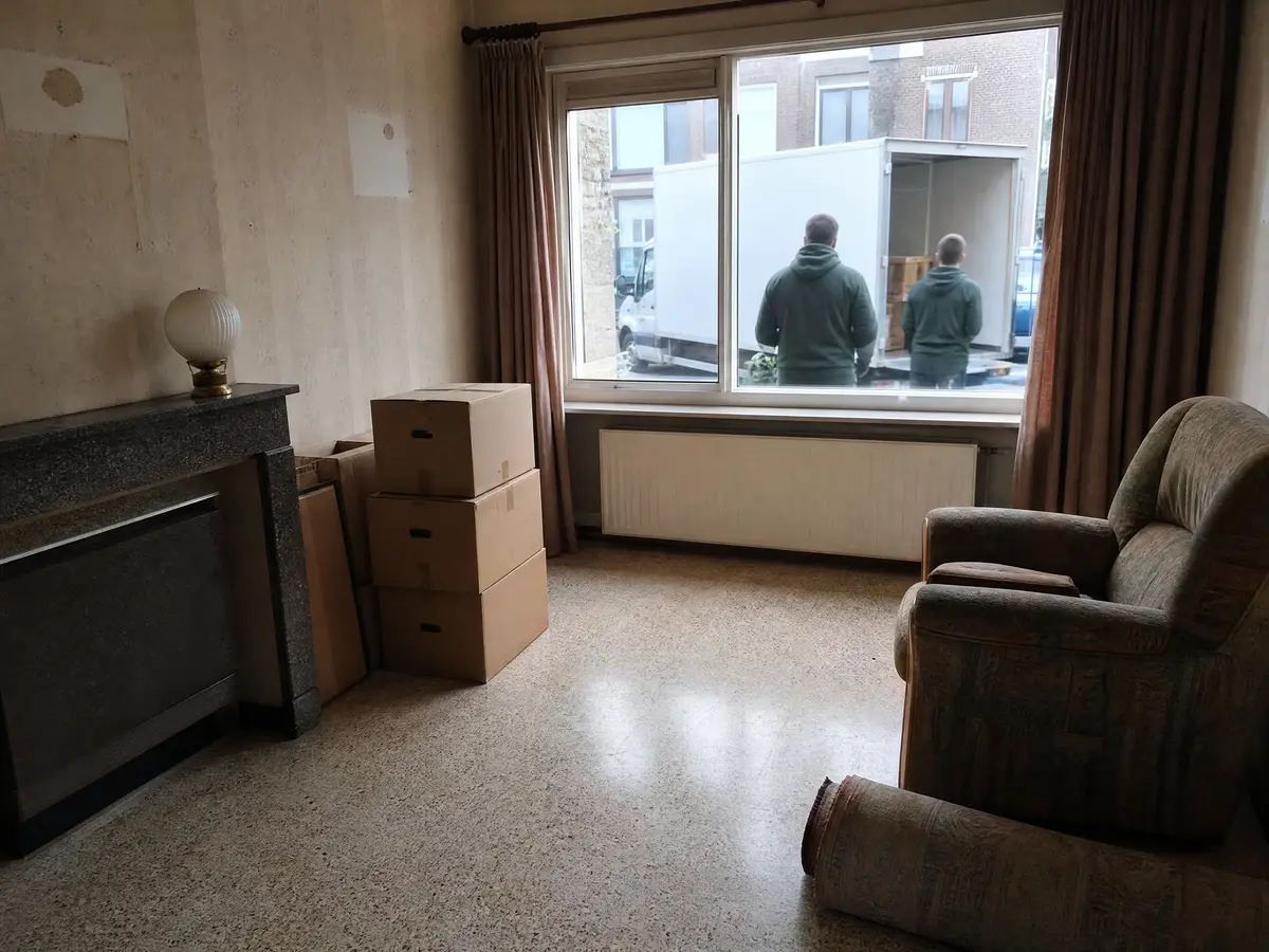 Half leeggemaakte woonkamer met dozen en een opgerold tapijt tijdens het leegmaken van een huis na een overlijden