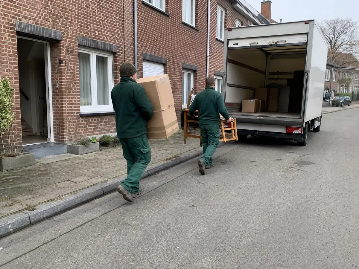 Twee medewerkers dragen dozen en een stoel uit een rijwoning naar een witte bestelwagen