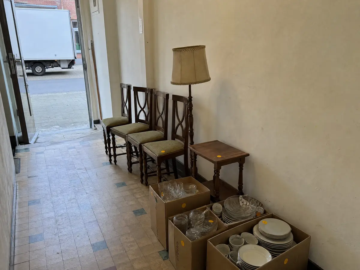 Stoelen, een lamp en dozen servies in een gang, klaar om naar De Kringwinkel te gaan