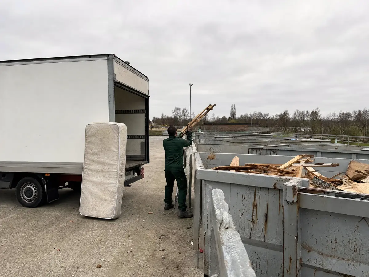 Een witte bestelwagen wordt per afvalsoort gelost aan de containers van een recyclagepark